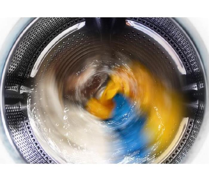 view of brightly colored clothes on spin cycle in top loading washing machine
