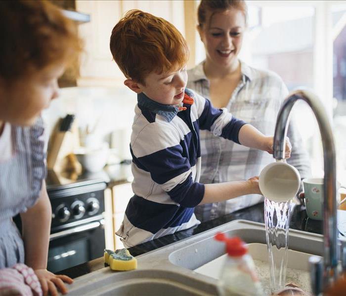 Two children and their Mother washing the dishes in the kitchen sink.